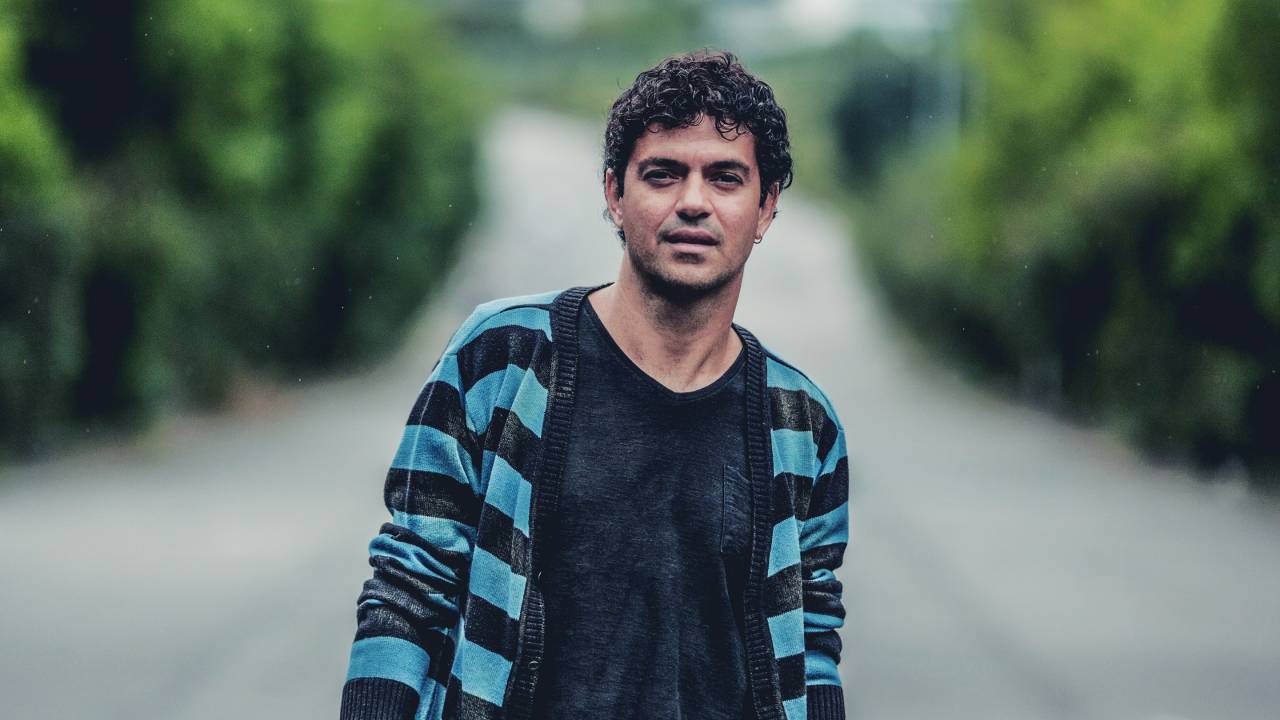 Jorge Vercillo numa rua deserta e arborizada, sorrindo
