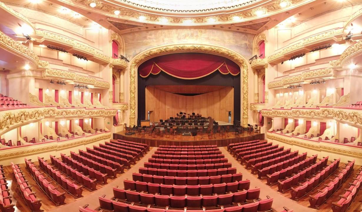 plateia vazia do theatro municipal do rio. ao fundo, vê-se o palco com os assentos da orquestra