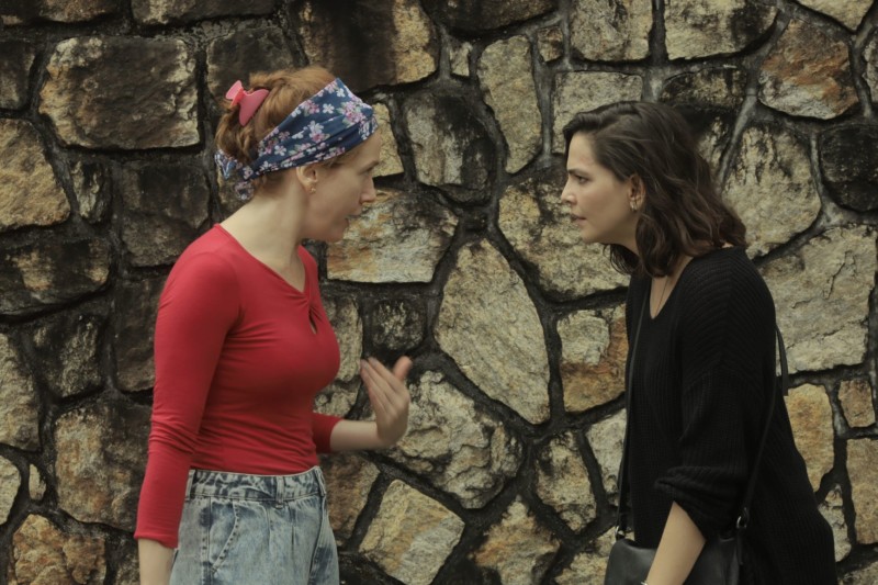 bom dia, verônica Personagens de Camila Morgado e Tainá Muller conversam em frente a um paredão de pedra