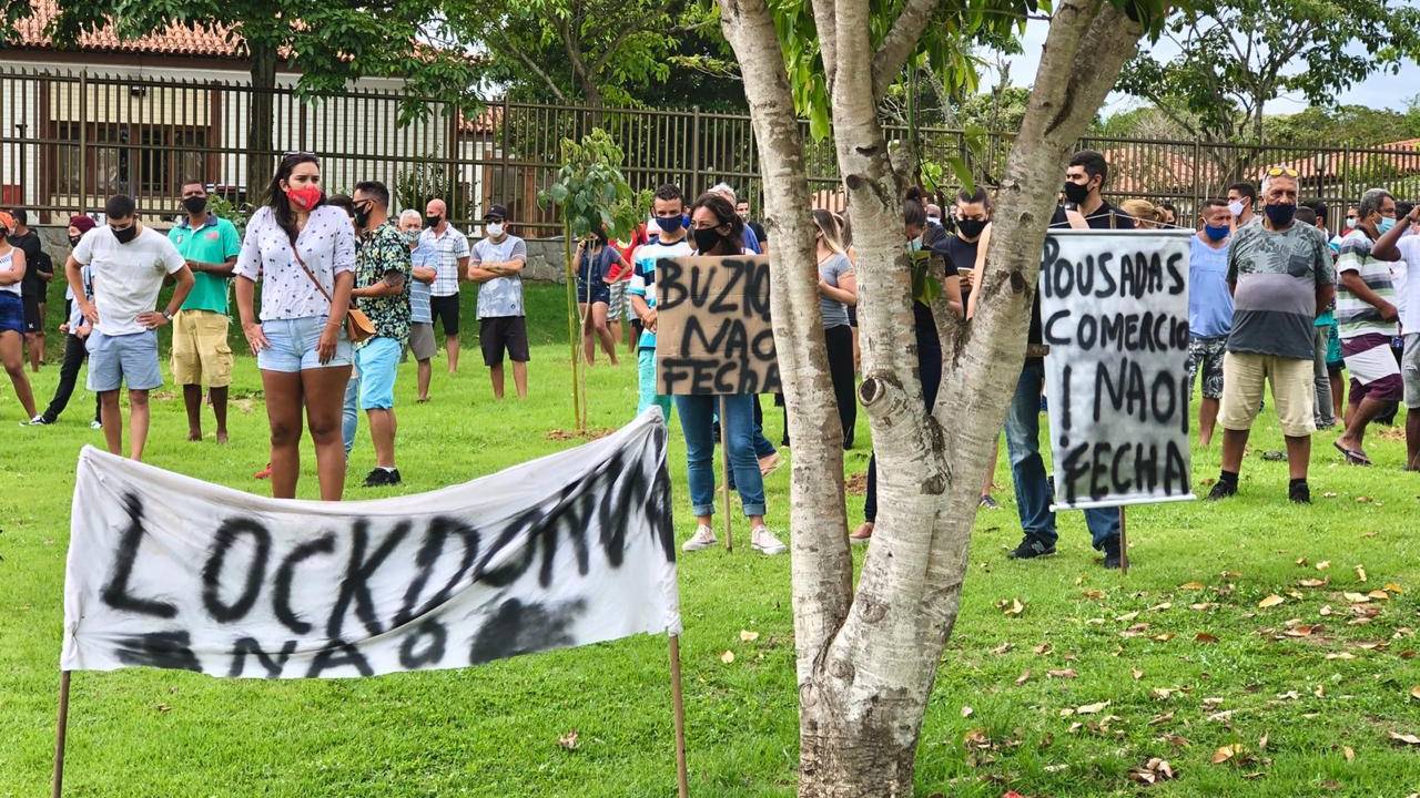 A imagem mostra manifestantes com placas de Lockdown Não num gramado em frente ao fórum de Búzios