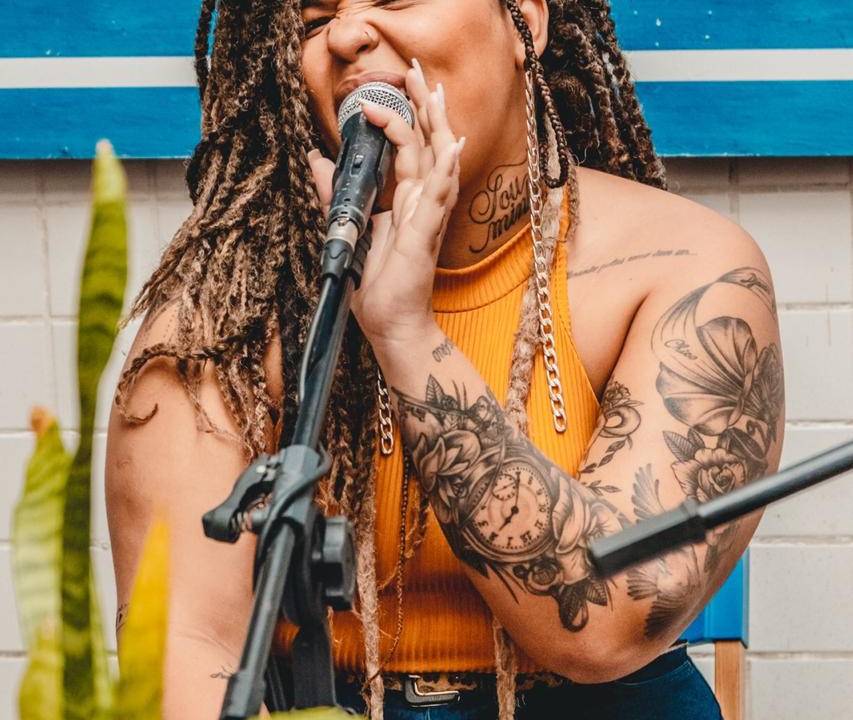 Cantora negra e tatuada, de dreds, empunha microfone