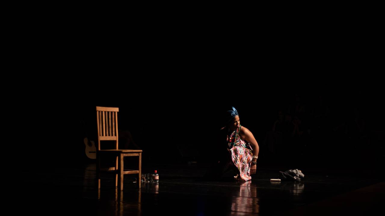 Atriz negra, com turbante, em cena, no palco