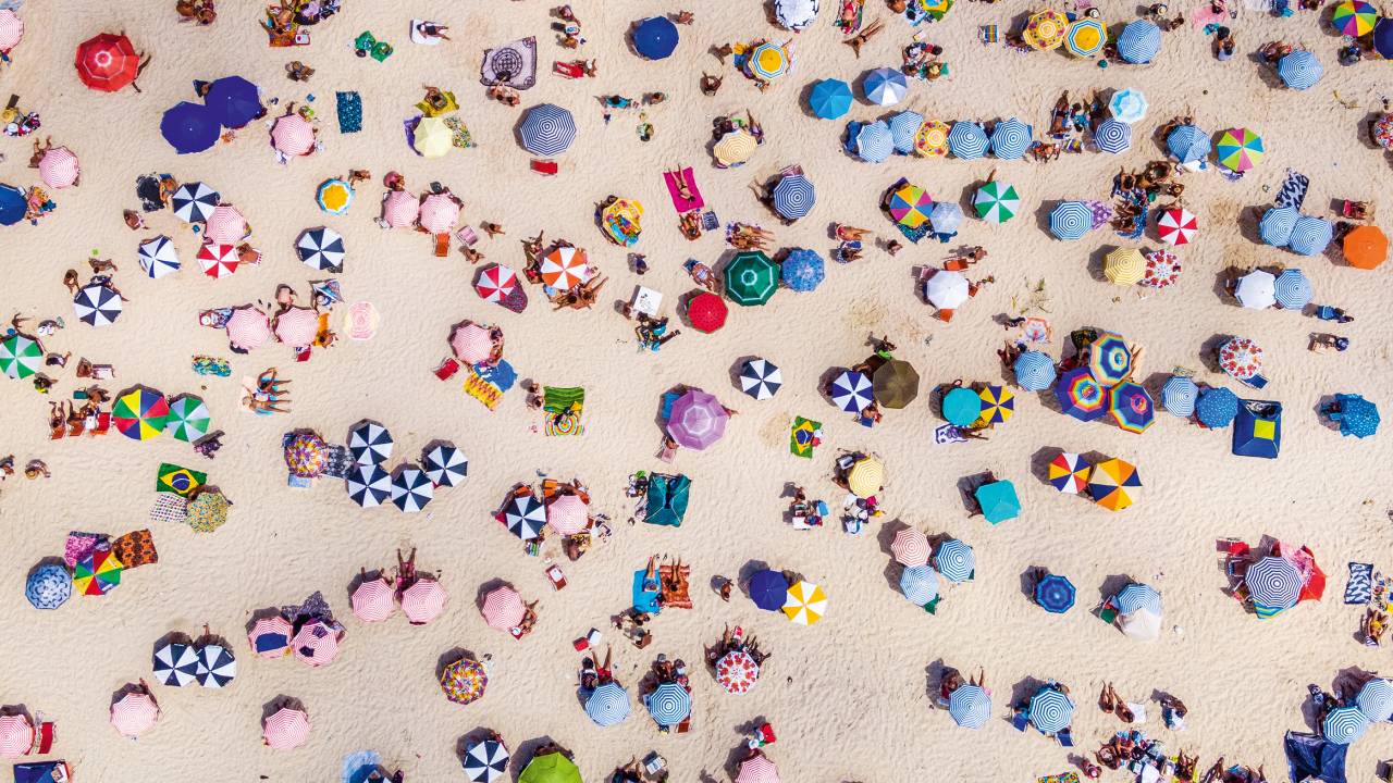 A imagem mostra a Praia de Copacabana repleta de guarda-sóis