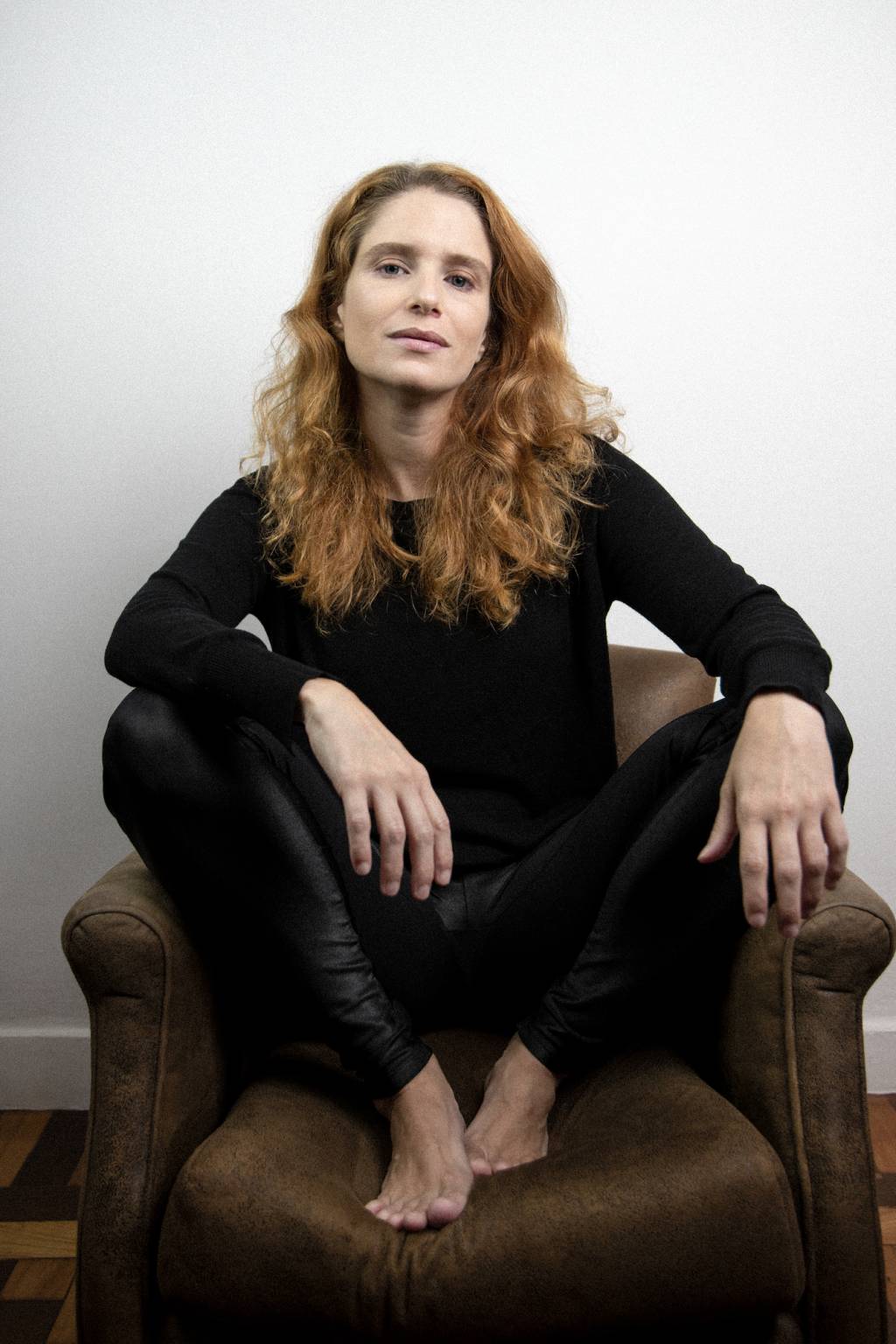 Julia Lund Atriz Julia Lund sentada numa poltrona, com os pés em cima do móvel