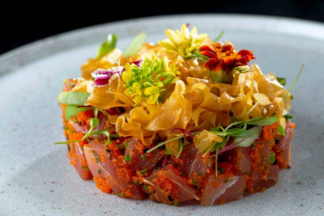 A imagem mostra um tartare de atum coberto de chips de gengibre e flores comestíveis