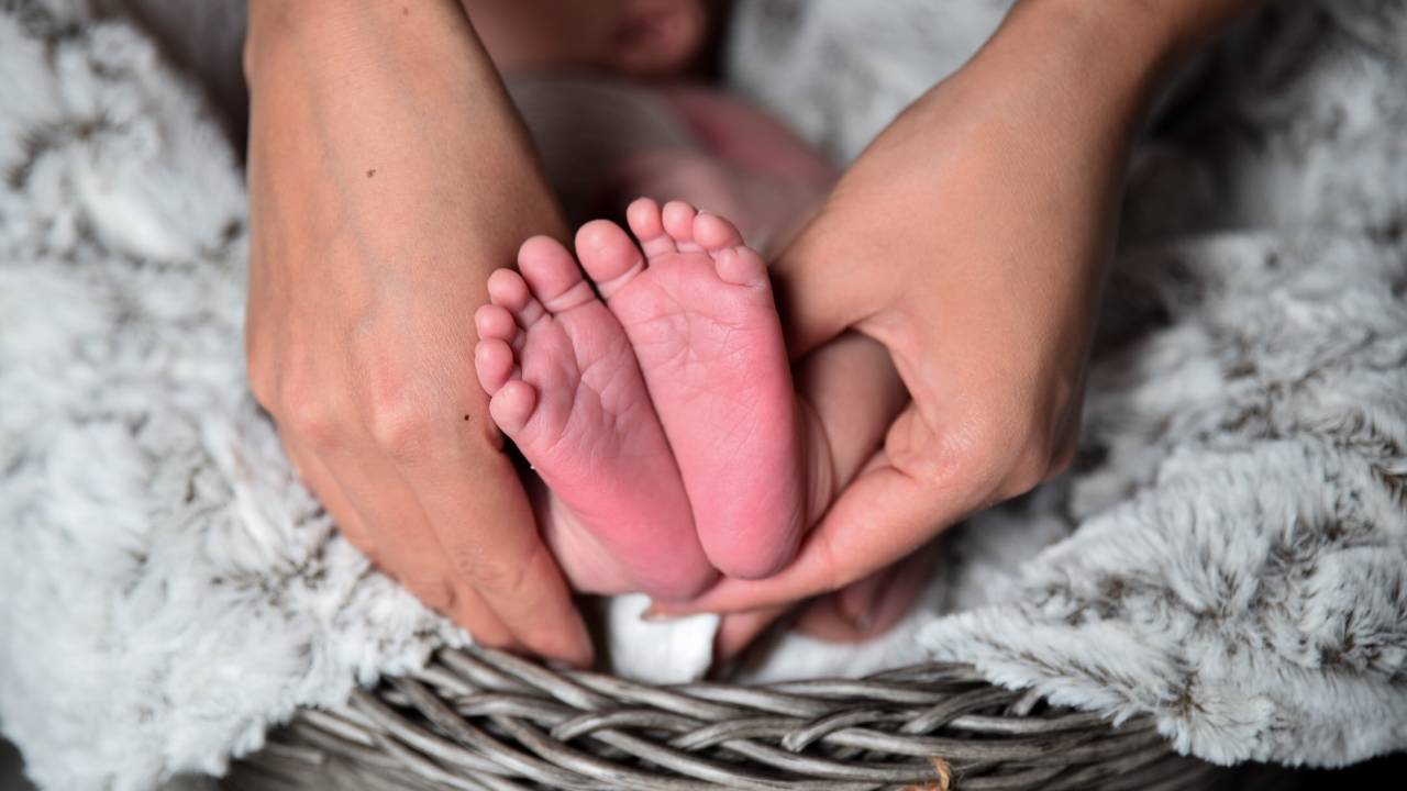 A imagem mostra o pé de um recém-nascido segurado pelas mãos da mãe