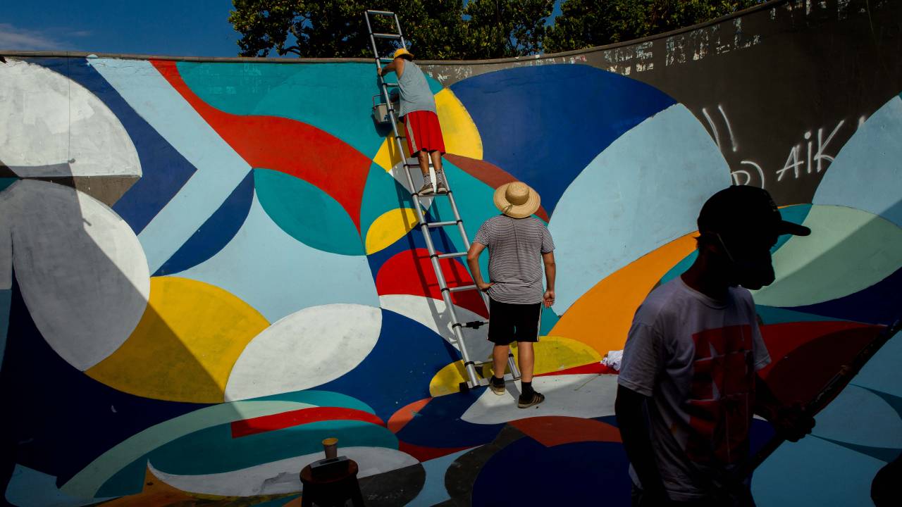 A imagem mostra duas pessoas pintando a pista de skate do arpoador com cores vivas