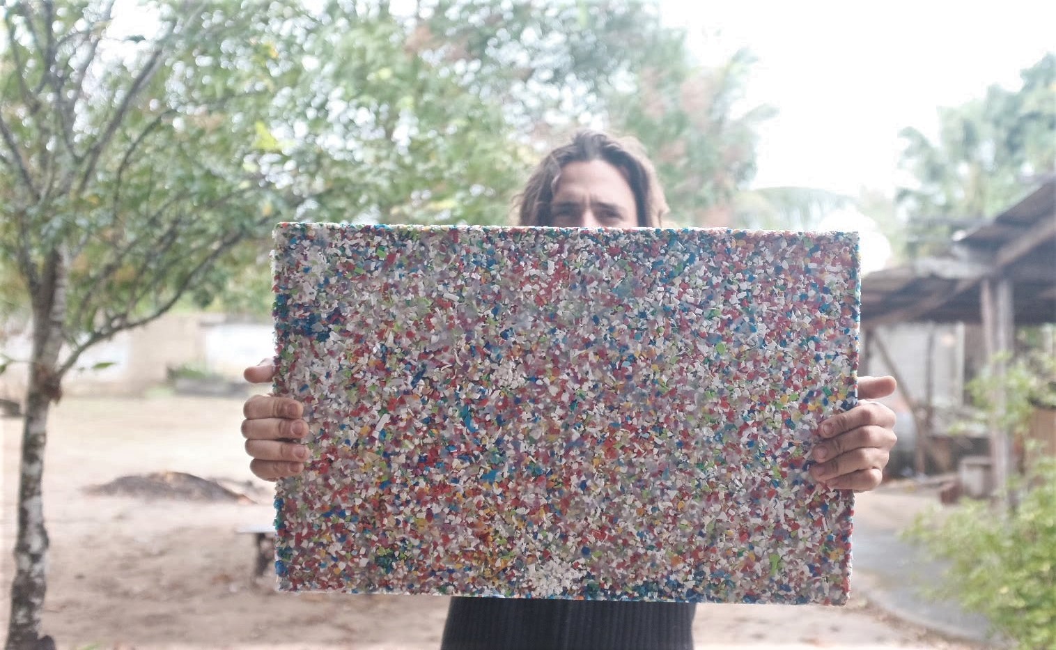 Homem segura placa com peda&ccedil;os de pl&aacute;stico triturados e prensados