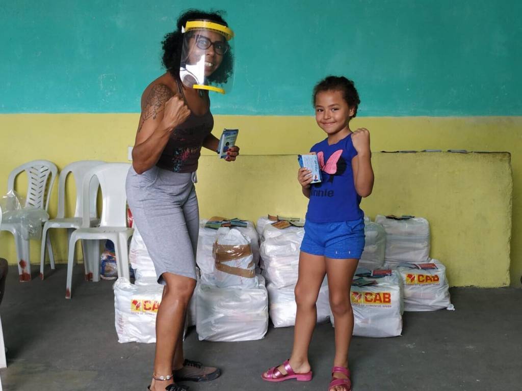 Foto 3 – Divulgação Imagem mostra uma mulher e uma menina em frente a cestas básicas