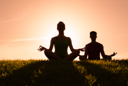 Imagem mostra a silhueta de duas pessoas meditando