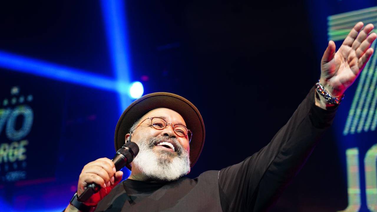Jorge Aragão sorrindo no palco, com o microfone na mão