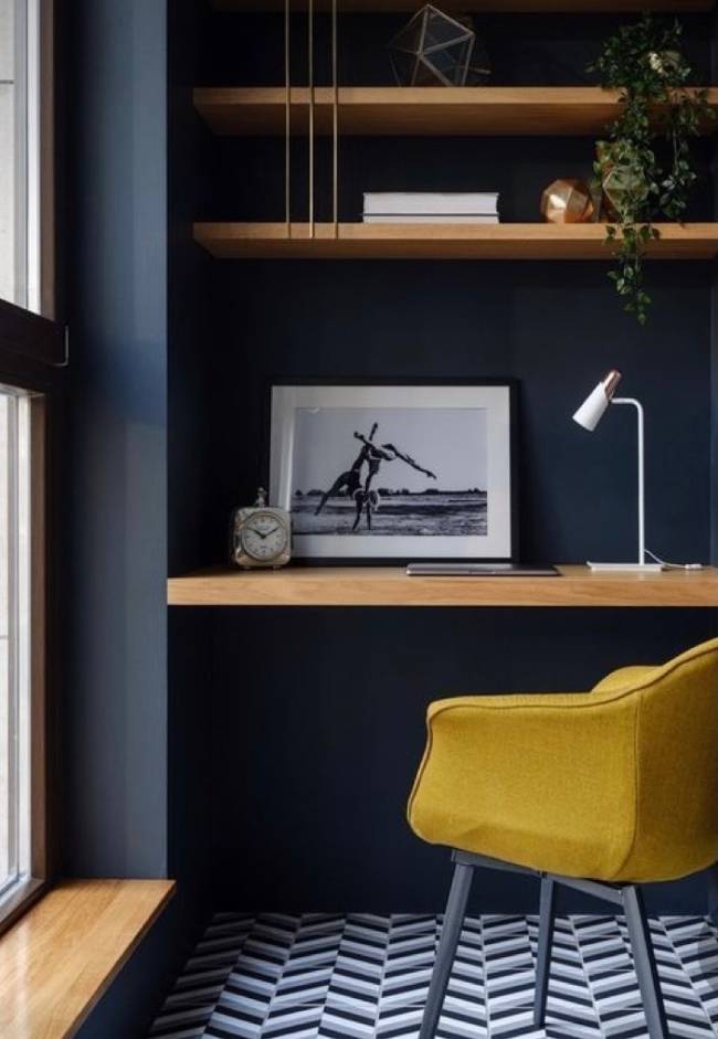 A imagem mostra um pequeno home office com parede azul e em segundo plano uma cadeira com estofado amarelo