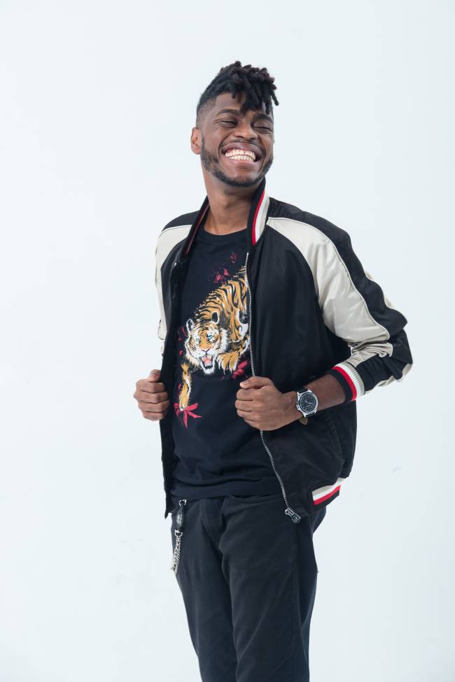 Yuri Marçal Yuri Marçal aparece usando uma blusa com um tigre estampado e uma jaqueta preto e branca com um grande sorriso no rosto