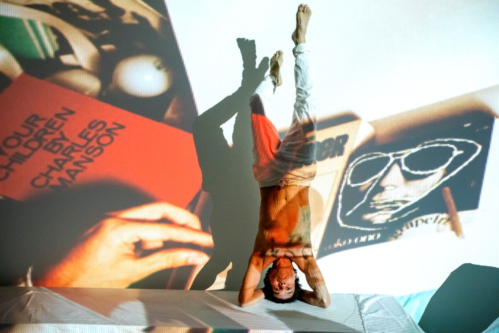 O diretor artístico do Centro Cultural Hélio Oiticica, César Oiticica Filho, está de cabeça para baixo, plantando bananeira, com projeções em uma obra de Hélio Oiticica sobre ele