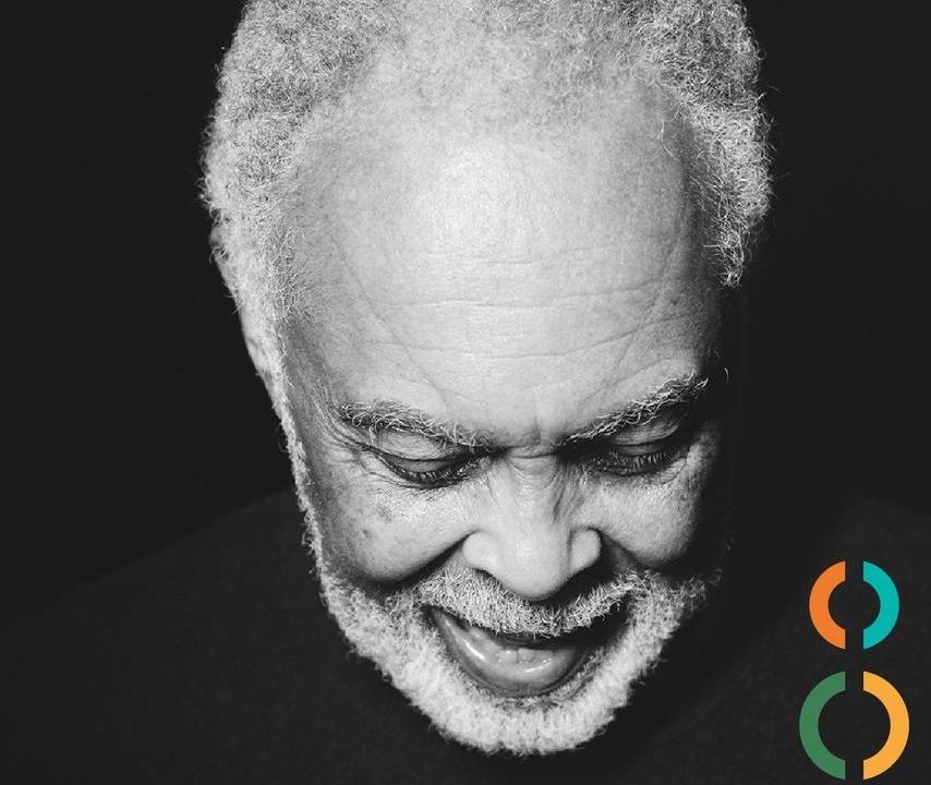 Foto em preto e branco do rosto de Gilberto Gil, com o artista olhando para baixo. Ao lado direito, embaixo, a logomarca comemorativa dos 80 anos