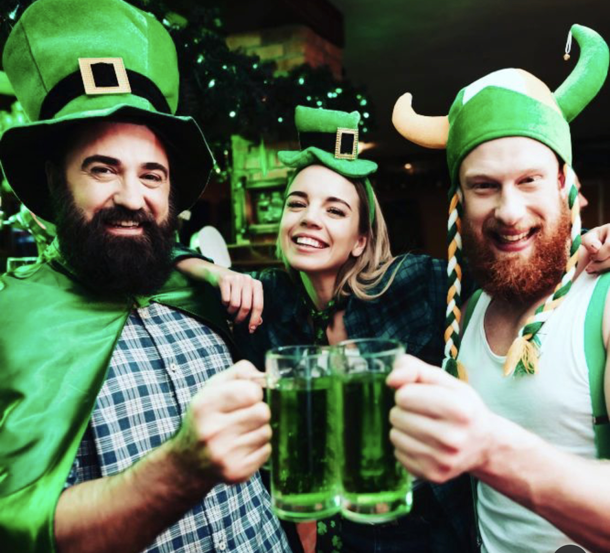 Foto mostra tr&ecirc;s pessoas com chap&eacute;us verdes segurando tr&ecirc;s chopes verdes