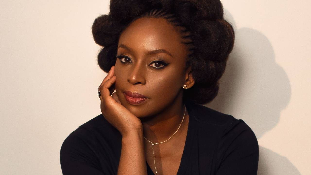 Chimamanda com a mão direita apoiada no queixo. Ela usa o cabelo com penteado afro com desenhos circulares.