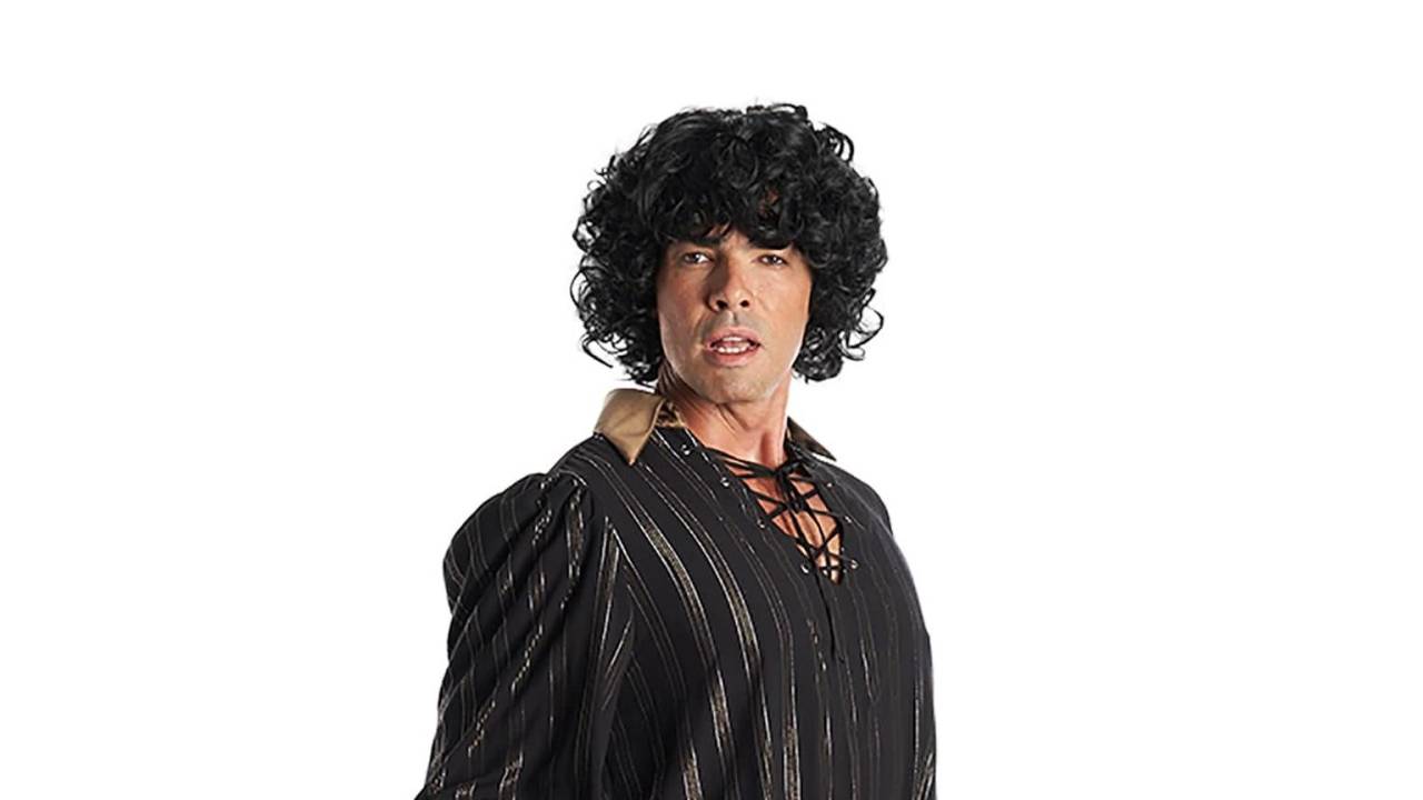 O ator Márcio Louzada caracterizado como Sidney Magal, com peruca de cabelos pretos cacheados, camisa preta com amarração na frente e gola bege.