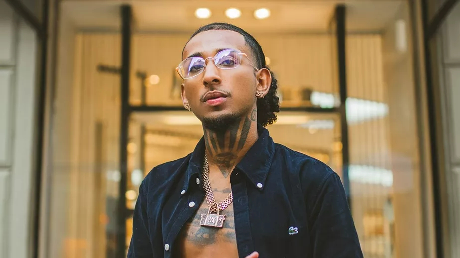 O artista MD Chefe é negro e tem cabelos compridos, que estão presos em um rabo de cavalo, além de cavanhaque e um bigode fino. Ele usa óculos de grau, jaqueta azul-marinho aberta, mostrando as tatuagens que tem no peito e no pescoço, e um cordão de outro.