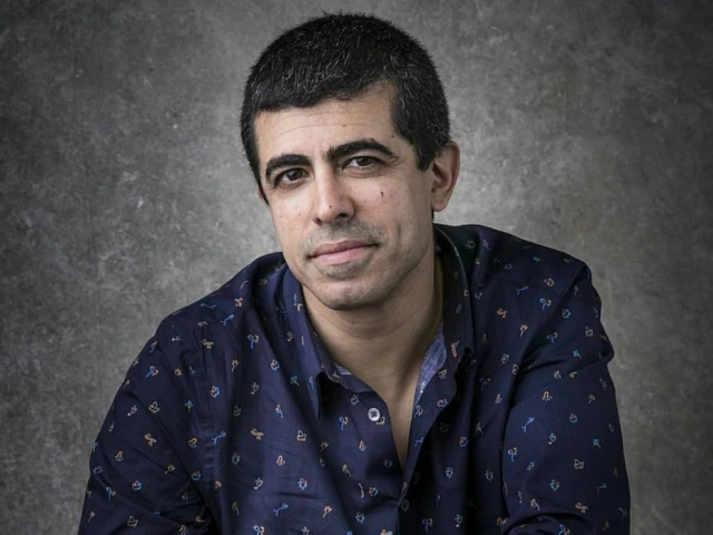 Marcius Melhem de paletó e camisa azul-escuro estampados sobre fundo cinza