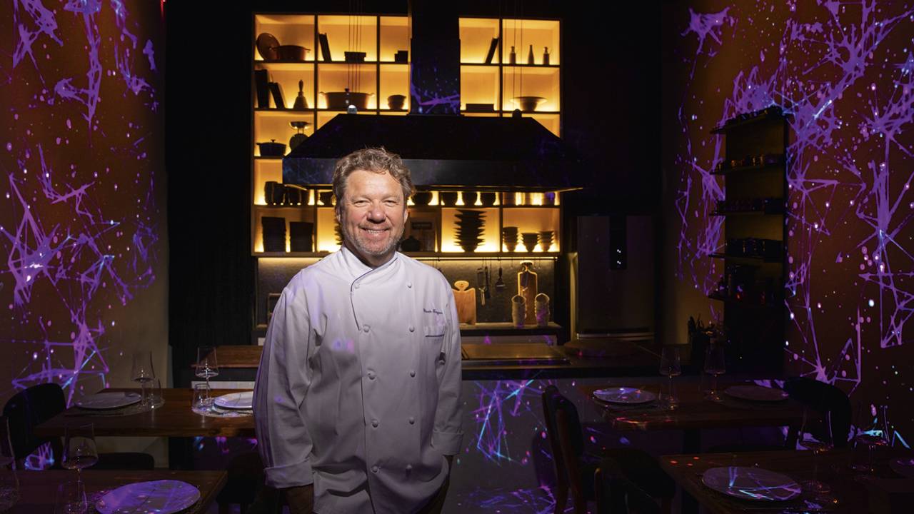 Claude Troisgros posa para a foto usando roupa de chef branca. Ele sorri