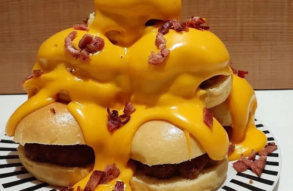 Torre de cinco hambúrgueres com molho de cheddar e bacon.