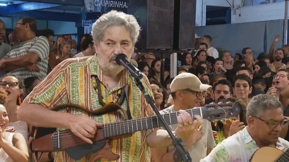 Foto mostra Moacyr Luz tocando e cantando em roda de samba