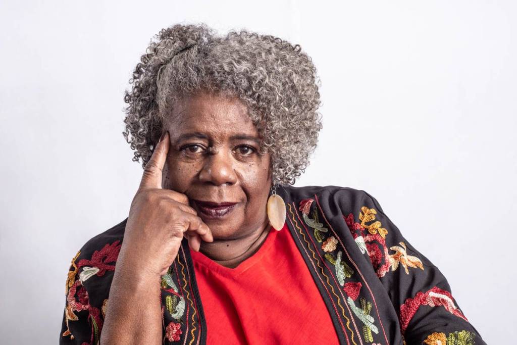 Conceição Evaristo_maio CCBB Aline Macedo Conceição Evaristo é uma mulher negra, de cabelos grisalhos crespos de tamanho médio. Ela veste blusa vermelha e camisa marrom estampada por cima. Ela olhando para a câmera e tem o dedo indicador da mão direita apoiado no rosto.