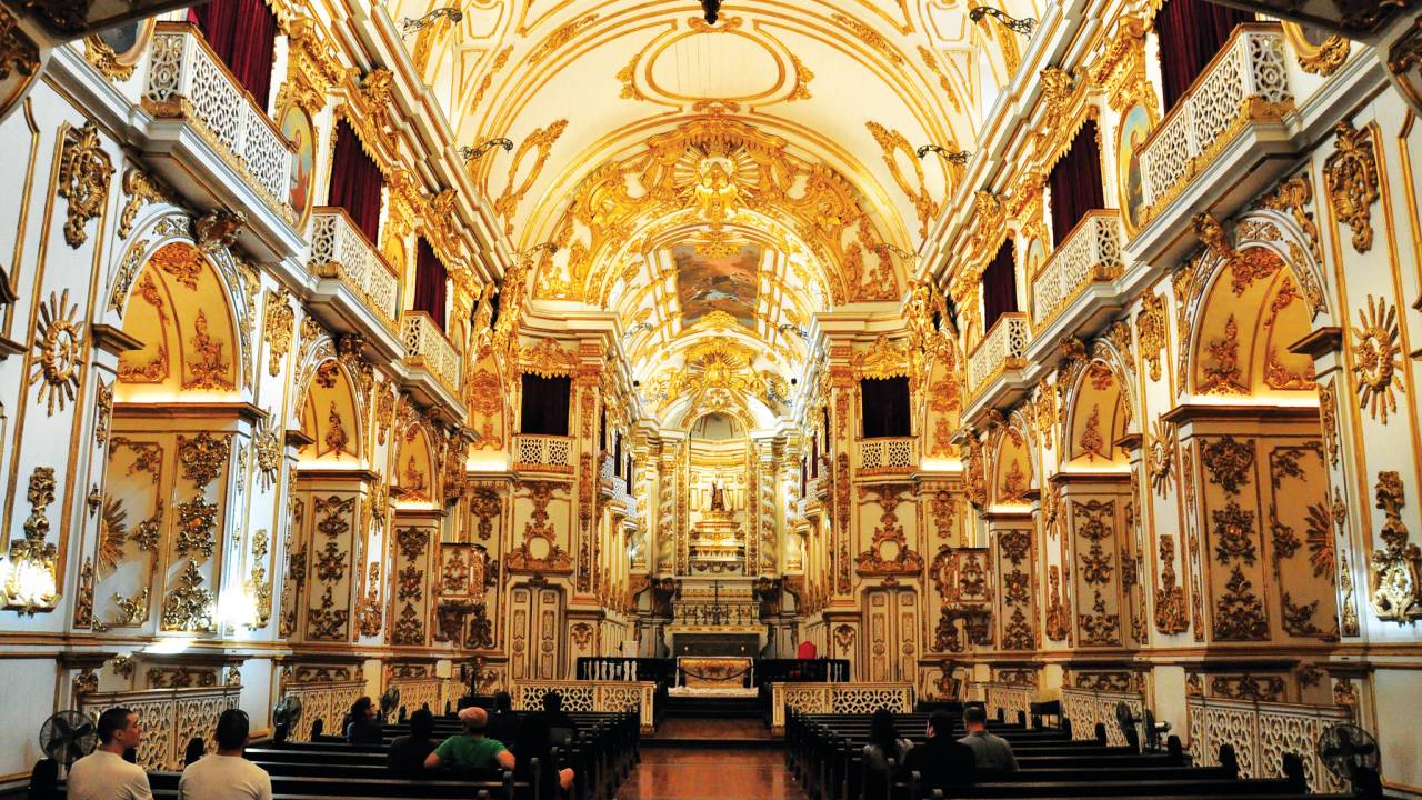Vista da Antiga Sé de quem está de frente para o altar, com bancos de madeiras e paredes brancas com detalhes em ouro
