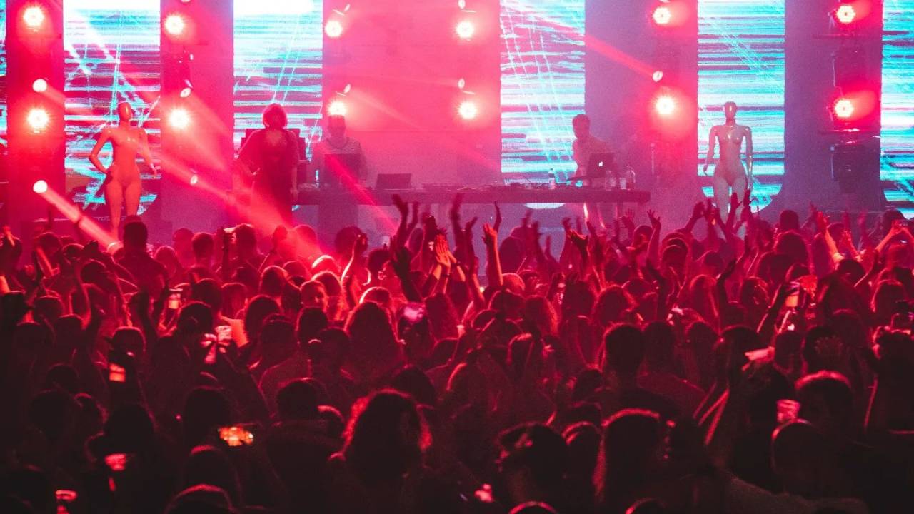 Luzes coloridas sobre a plateia diante de um palco com grandes janelas