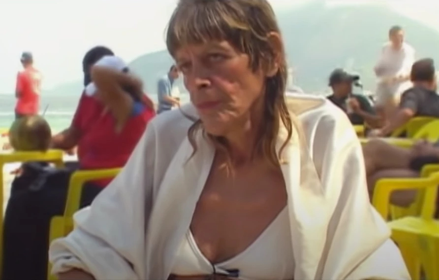 Uma mulher branca e com cabelos claros, com parte de cima de biquíni branca e camisa branca por cima