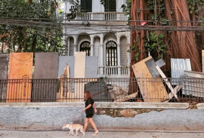 Mulher passeia com seu cão em frente a uma casa abandonada e antiga