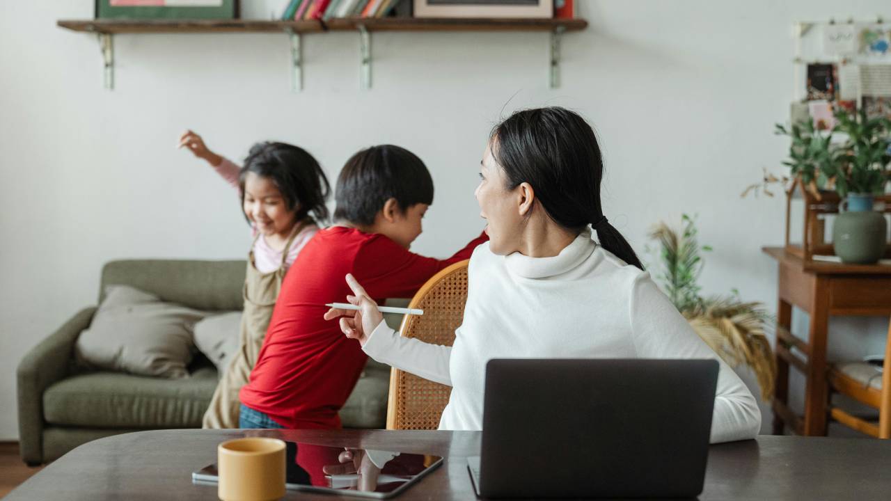 Uma mãe sentada tentando trabalhar e educando os filhos ao mesmo tempo