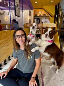 Patas e Rolhas_Gabriela Mulher sorrindo com dois cachorros ao lado